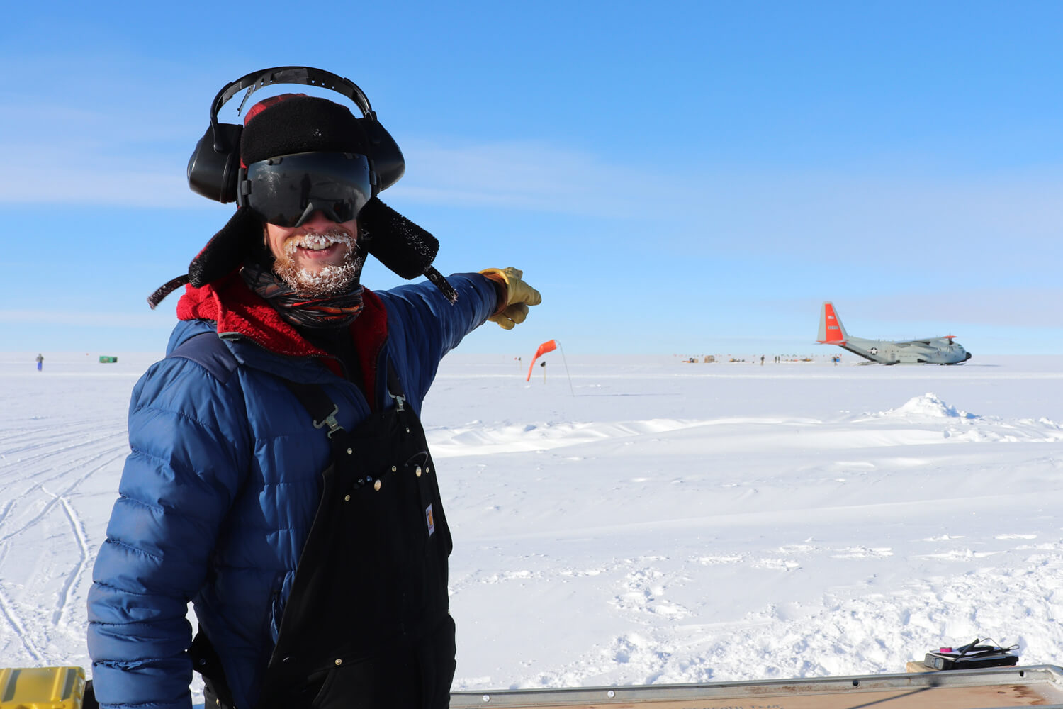 scientist pointing to an LC-130 aircraft on the skiway at Hercules Dome, Antarctica